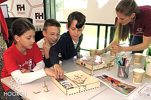 3 Volksschul-Kinder und eine Lehrerin spielen mit der Hoorch-Box beim eBazar 2025